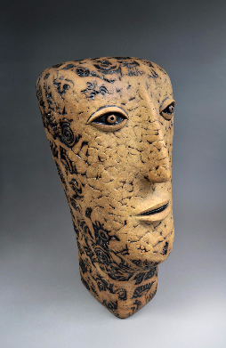 Elongated statue of a head, almost half a meter tall. Made with overlapping scales of clay, each stamped with a abstract pattern that has a rough texture.